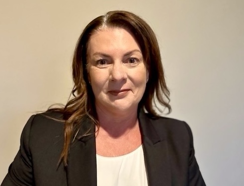 A woman with dark brown hair wearing a white blouse under a black business jacket